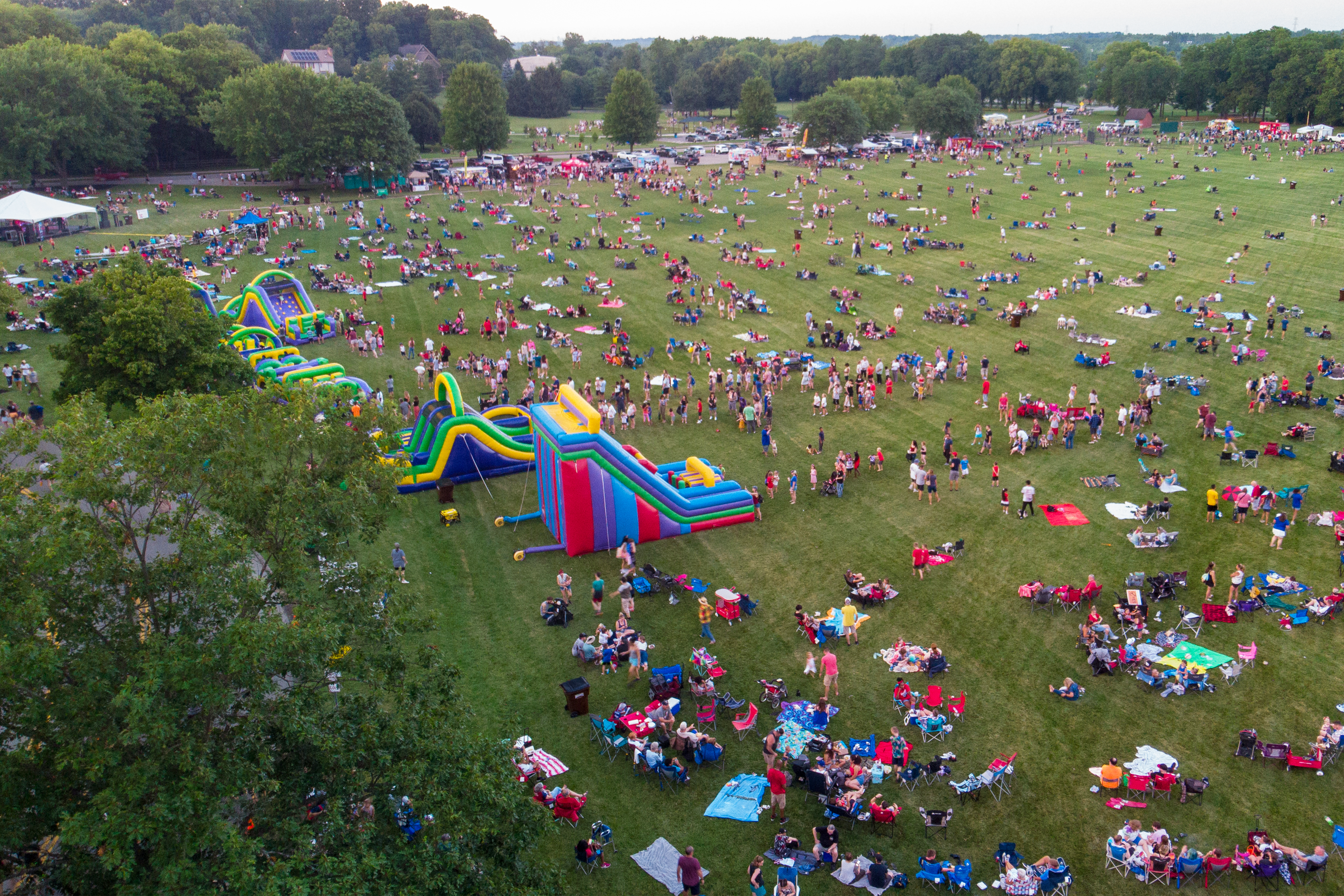 Drone shot of bouncy houses and many people sitting on field of Rotary Park at 4th of July event.